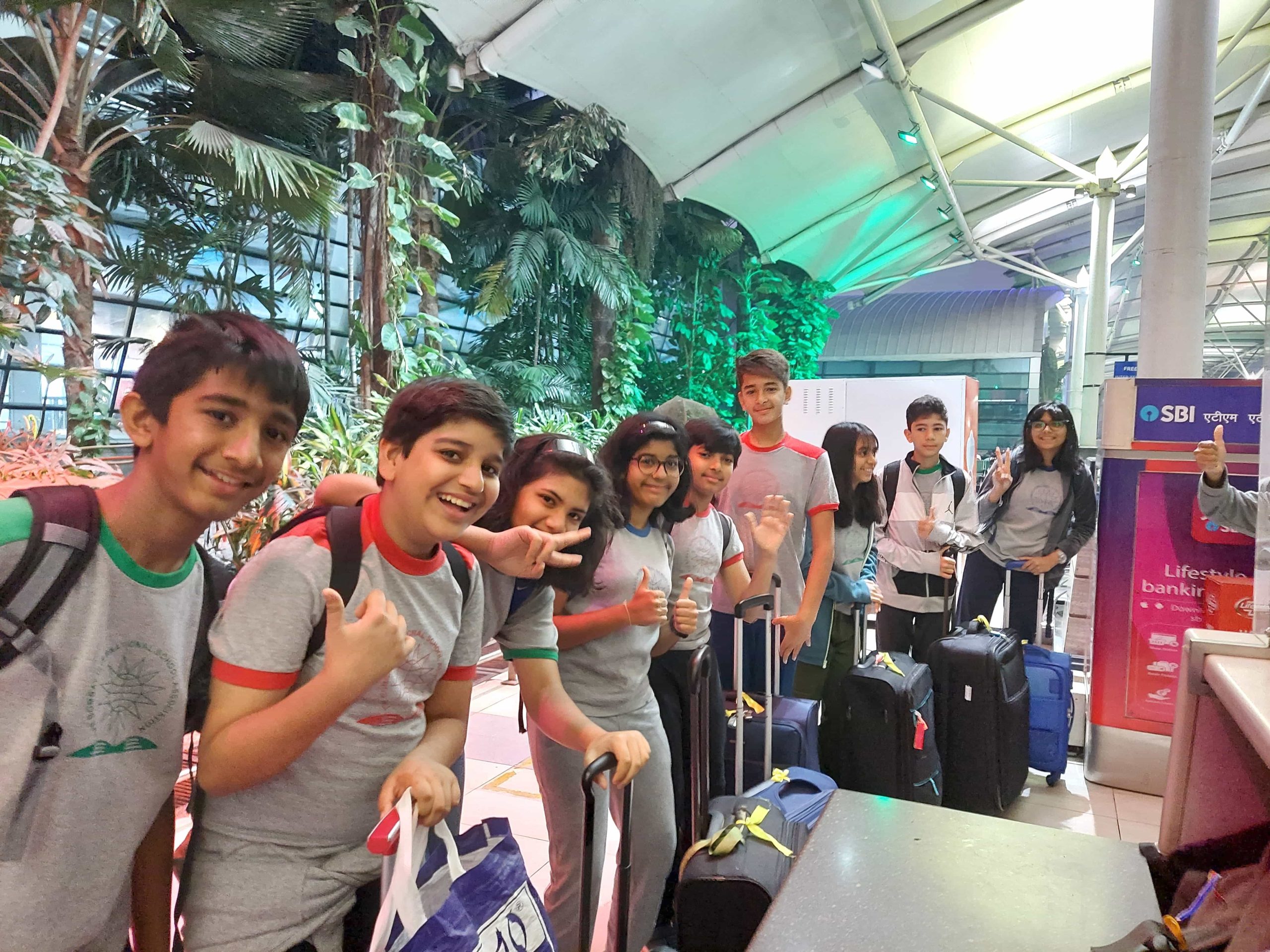 students in a line with their heavy luggage bags posing for camera as they are about to board onto a bus